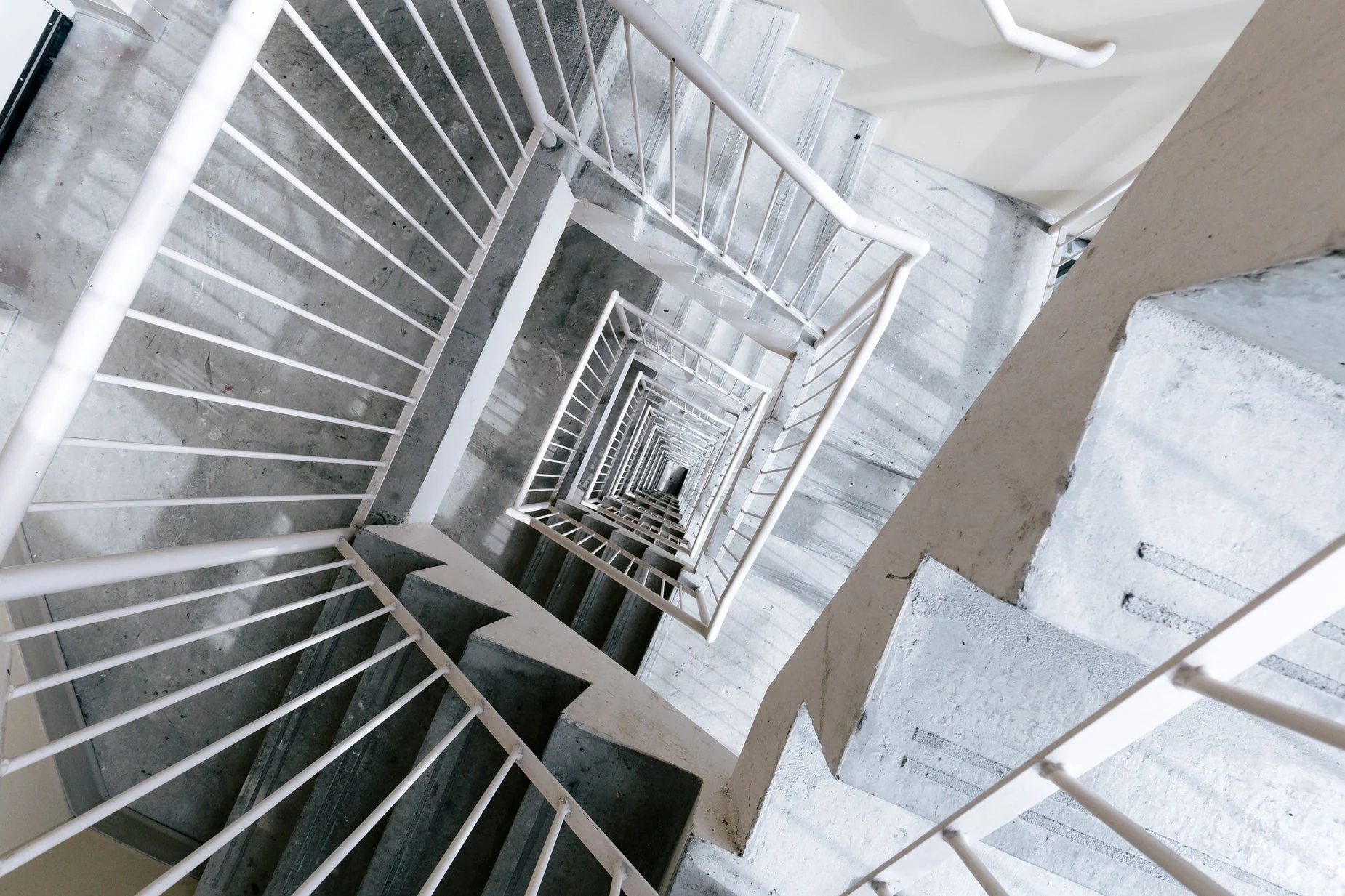 Looking down multiple concrete stair flights with round white metal handrails; photograph by Mitul Shah